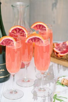 three glasses filled with pink wine and garnished with orange slices next to a bottle of champagne