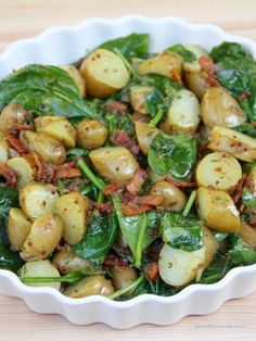 spinach and potato salad with bacon in a white bowl on a wooden table top