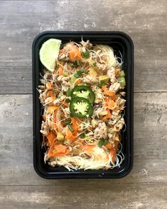 a black container filled with food on top of a wooden table next to a slice of lime