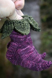 someone holding up a purple and green knitted mitt with leaves on the top