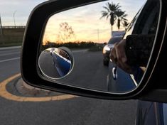 a car's side view mirror is shown with palm trees in the background