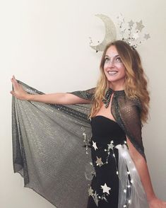 a woman in a black and silver dress is holding up a sheer shawl with stars on it