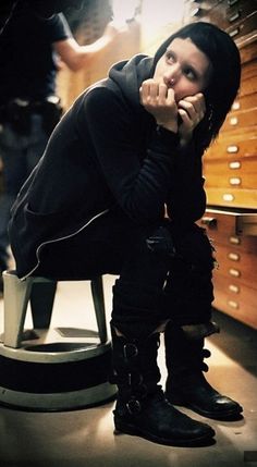 a man sitting on top of a chair in front of a wooden shelf filled with drawers