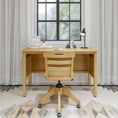 a wooden desk sitting in front of a window next to a chair and lamp on top of a rug