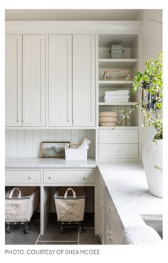 a kitchen with white cabinets and two baskets on the counter, next to a vase filled with flowers