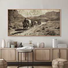 an old photo of horses and riders in the desert on a wall above a sideboard