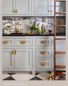 a kitchen with marble counter tops and gold pulls on the cabinet doors, next to a ladder