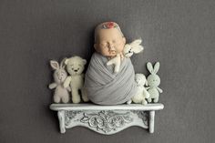 a baby wrapped in a blanket is sitting on a shelf with stuffed animals around it