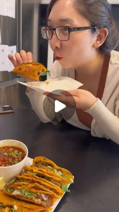 a woman in glasses is eating some tacos and salsa at a restaurant counter top