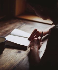 a person sitting at a table with a book and pen in their hand, writing