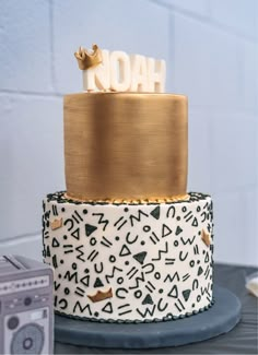 a three tiered cake decorated with black and white designs, gold accents and the word noah on top