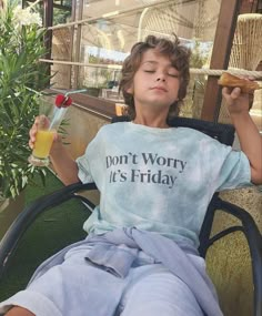 a young boy sitting in a chair holding a drink