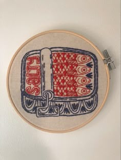 an embroidered wall hanging with a red and blue train on it's side, next to a white wall