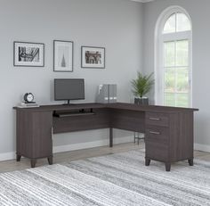 a corner desk with a computer on it in front of a large window and rug