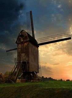 an old windmill sitting on top of a lush green field under a cloudy sky at sunset