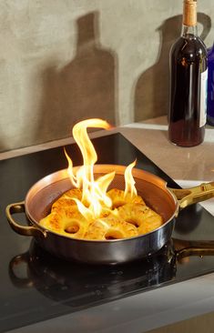 a skillet with food cooking on top of a stove next to a bottle of wine