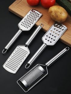 four kitchen utensils on a cutting board with tomatoes, cucumbers and potatoes