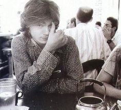 two women sitting at a table with cups and tea kettles on it, one is covering her face