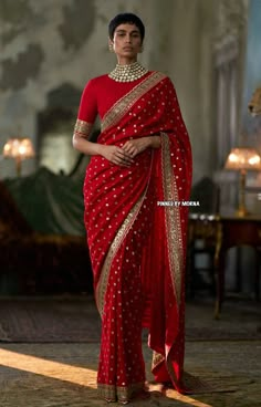 a woman in a red sari with gold accents on her head and shoulders, standing in