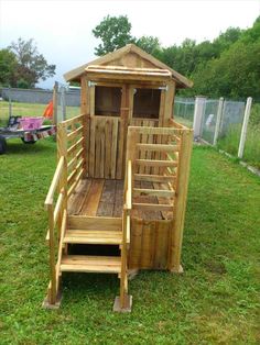 a small wooden structure with stairs and steps on the grass in front of a fence