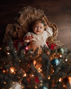 a baby laying on top of a christmas tree next to a pile of ornaments and lights