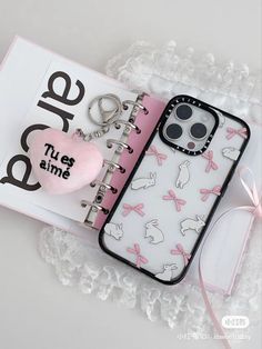 a phone case with a heart and keychain on it next to a book