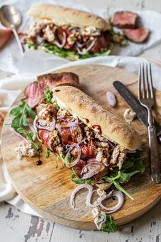 a sandwich with meat, onions and lettuce on a cutting board next to silverware