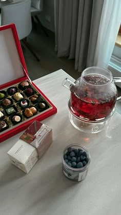 a glass teapot filled with chocolates next to a box of candies on a table