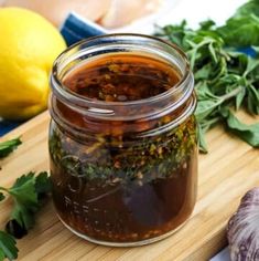 a wooden cutting board topped with a jar of pickles and herbs next to lemons