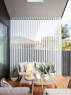 an outdoor living area with wooden flooring and white blinds on the side of the building