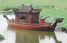 a wooden boat floating on top of a river next to lush green field covered in grass