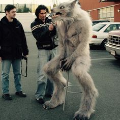 two men standing next to each other in a parking lot with an animal on top of a chair