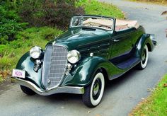 an old green car is parked on the side of the road