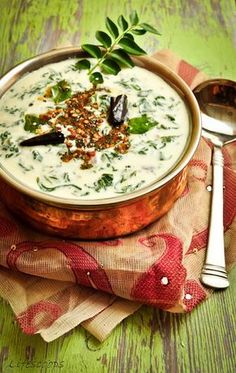 a metal bowl filled with soup on top of a wooden table next to a spoon