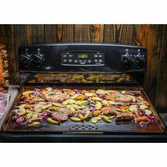 an open oven with food cooking on the grill in front of it, including steaks and vegetables