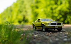 a toy car sitting on the side of a road near some grass and trees in the background