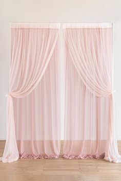 two pink drapes hanging on the side of a wall next to a wooden floor