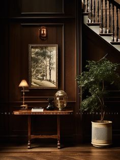 a table with a lamp and a painting on the wall next to a stair case