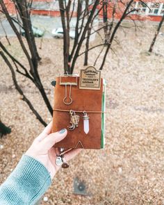 a person holding up a small brown book with charms on it and a tree in the background