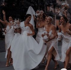 a group of bridesmaids in white dresses walking down the street with their arms in the air