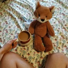 a teddy bear sitting on top of a bed next to a cup of coffee