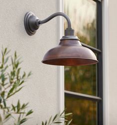 an outdoor light on the side of a building next to a tree and potted plant