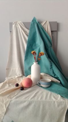 a white vase sitting on top of a bed next to two peaches and other fruit