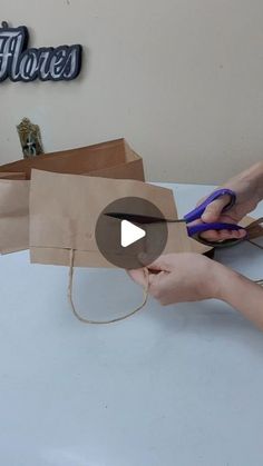 a person cutting paper with scissors on top of a white table next to a brown bag