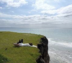 a man laying on top of a lush green field next to the ocean