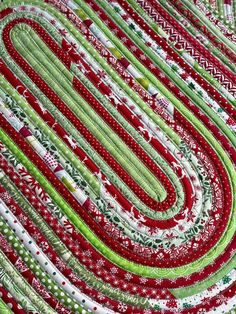 a quilted table runner with red and green designs on it's edges, in the shape of a spiral