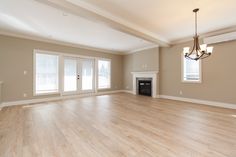 an empty living room with hard wood floors and white trim around the fireplace, windows, and french doors