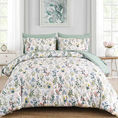 a bed with floral comforter and pillows in a room next to a painting on the wall