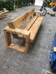 a wooden bench sitting on top of a brick road next to a blue dumpster