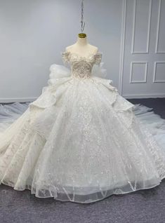 a white wedding dress on display in a room with grey carpet and walls behind it